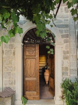 Green grapes weave over the arched entrance to an ancient building with a wooden door. High quality photo