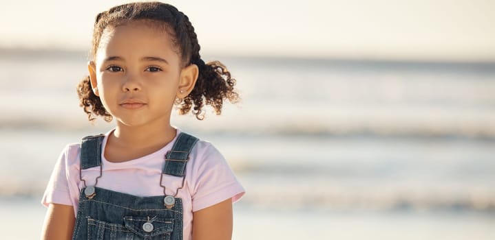 Portrait of girl child on holiday, at beach and standing in the sun by the ocean. Kid on summer holiday, travel to the coast in the sunshine and sand. Toddler by sea, childhood memory and on vacation.