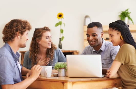 A group of friends sitting together in a coffee shop with a laptop.