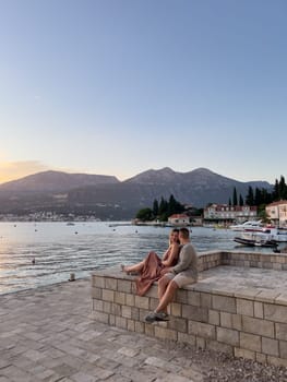 Man hugs woman, sitting on a stone fence on the shore of an old town. High quality photo