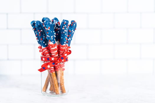 Homemade chocolate-covered pretzel rods decorated like the American flag in a glass jar.