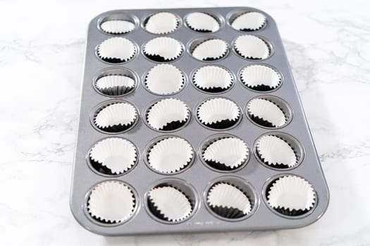 Scooping cupcake batter with dough scoop into a baking pan with liners to bake American flag mini cupcakes.