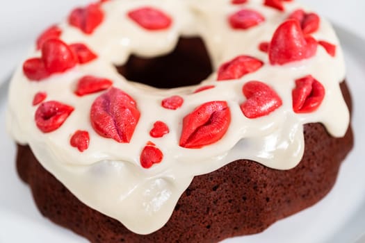 Freshly baked red velvet bundt cake with chocolate lips and hearts over cream cheese glaze for Valentine's Day.