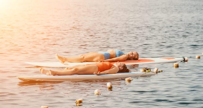 Woman sup yoga. Middle age sporty woman practising yoga pilates on paddle sup surfboard. Female stretching doing workout on sea water. Modern individual hipster outdoor summer sport activity