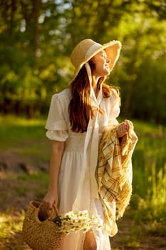 a happy woman in a light dress walks through the woods with a plaid and a wicker bag in her hands. High quality photo