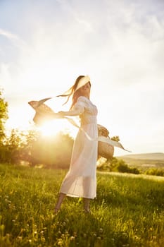 a woman in a light dress walks in nature holding a hat in her hands lit from the back by the sun. High quality photo