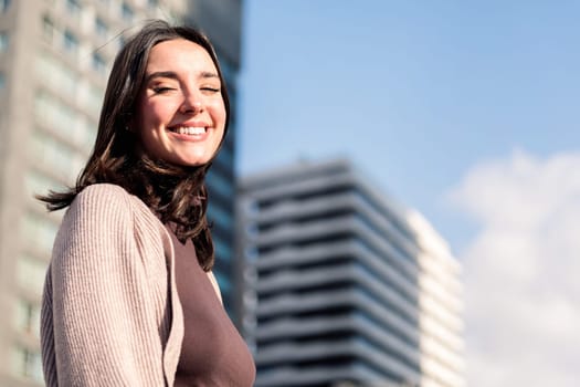 smiling young woman looking at camera on sunny day at city, concept of happiness and urban lifestyle, copy space for text