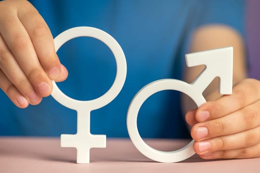 The concept of gender equality. Symbol of female and male gender in hand as a symbol of equality of rights. On a purple background in a blue t-shirt with copy space. High quality photo