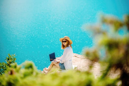 Freelance woman working on a laptop by the sea, typing away on the keyboard while enjoying the beautiful view, highlighting the idea of remote work