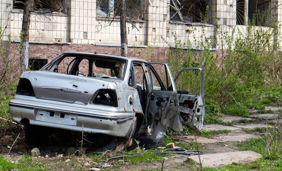 A broken car, shot by artillery, stands in the courtyard of a multi-storey residential building. War between Russia and Ukraine. The wreckage of an abandoned car