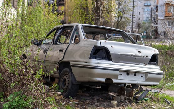 A broken Ukrainian civilian car, shot by artillery, stands in the courtyard of a destroyed house. War between Russia and Ukraine. The wreckage of an abandoned car