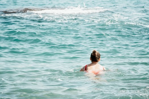 Young woman in red bikini on Beach. Girl lying on pebble beach and enjoying sun. Happy lady in bathing suit chilling and sunbathing by turquoise sea ocean on hot summer day. Close up. Back view