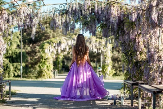 Woman wisteria lilac dress. Thoughtful happy mature woman in purple dress surrounded by chinese wisteria.