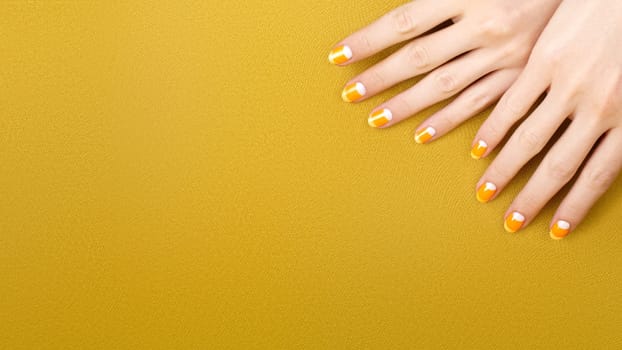 Beautiful Female Hands with bright Orange Manicure like Candy Corn on Yellow Background. Manicured Nails with Creative Gel Polish Design. Halloween Style