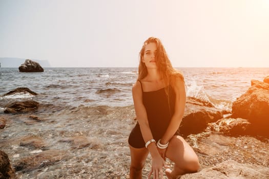 Woman travel sea. Young Happy woman in a long red dress posing on a beach near the sea on background of volcanic rocks, like in Iceland, sharing travel adventure journey