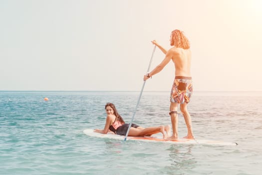 Silhouette of woman standing, surfing on SUP board, confident paddling through water surface. Idyllic sunset or sunrise. Sports active lifestyle at sea or river.