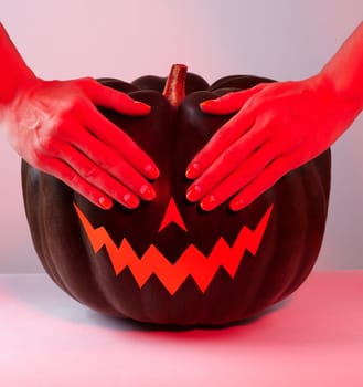 Halloween Pumpkin with Paper Cut Scary Face in red Light. Jack Halloween with hands on eyes. Smile Jack Pumpkin. Copy space