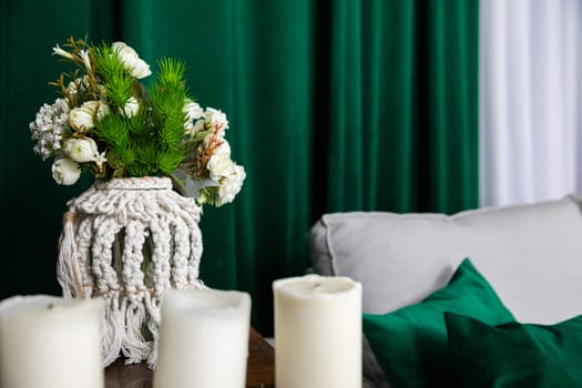 Flower decoration on the background of a green curtain standing right next to the sofa. The living room in the color scheme of gray and white and a definite dark bottle green.