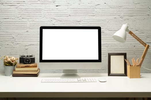 Front view of blank screen computer, camera, lamp, picture frame and books on white table.