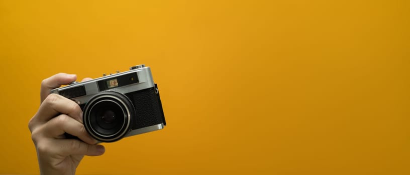 Image of hand holding vintage camera isolated on yellow background. Empty space for your advertising.