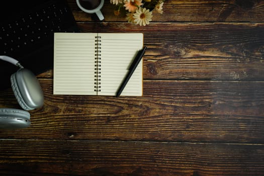 Top view of blank spiral notepad, pen, headphone and coffee cup on wooden table.