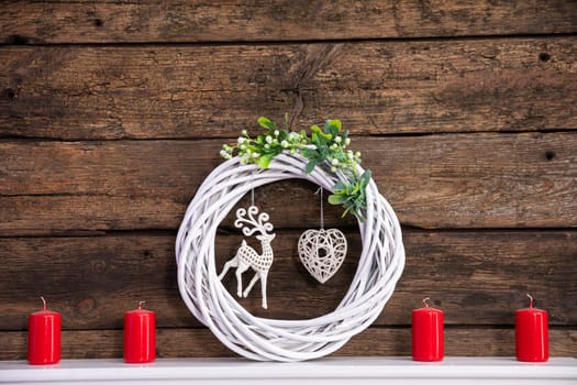 A modest decoration set on a white shelf for the duration of Christmas. Braided wicker garland in the center with a reindeer and a heart.