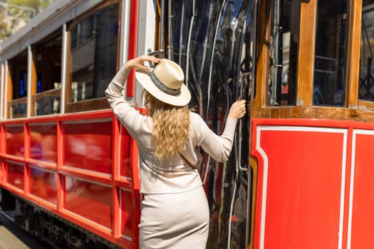 Beautiful young girl tourist in a hat poses in front of tram at popular Istiklal street in Beyoglu, Istanbul, Turkey .