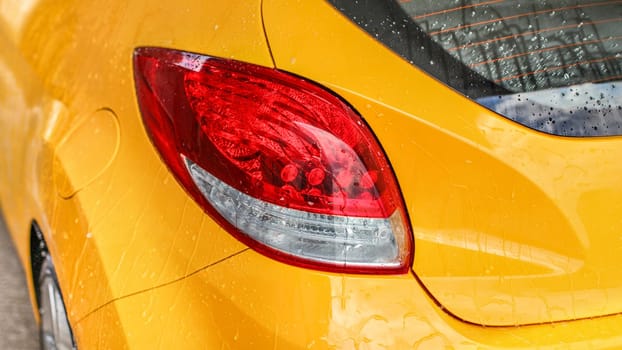 Rear light of yellow car covered with water when washed in carwash.