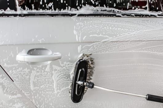 Side of silver car washed in self service carwash, brush cleaning shampoo foam.