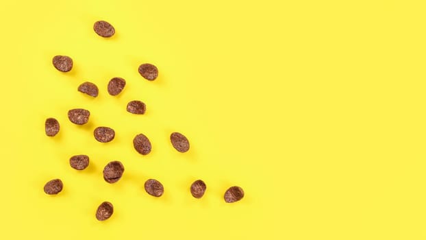 Tabletop view chocolate corn flakes scattered on yellow board, space for text on right side.