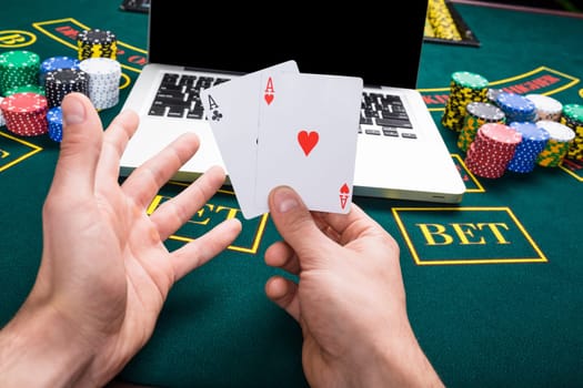 casino, online gambling, technology and people concept - close up of poker player with playing cards, notebook and chips at green casino table. first-person view. two aces, a winning combination