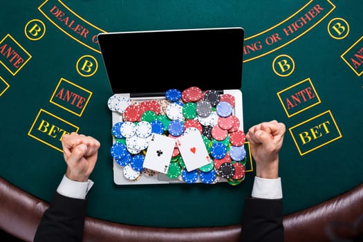 casino, online gambling, technology and people concept - close up of poker player with playing cards, laptop and chips at green casino table. top view