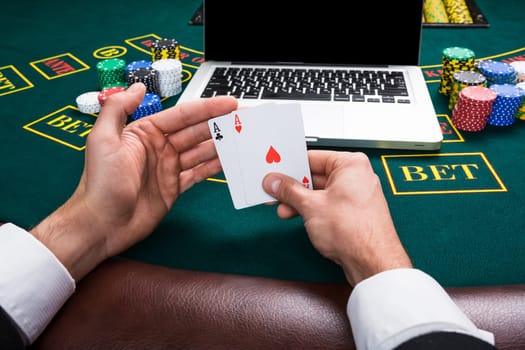 casino, online gambling, technology and people concept - close up of poker player with playing cards, notebook and chips at green casino table. first-person view. two aces, a winning combination