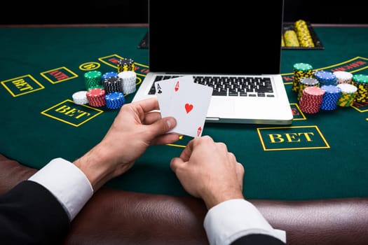 casino, online gambling, technology and people concept - close up of poker player with playing cards, notebook and chips at green casino table. first-person view. two aces, a winning combination