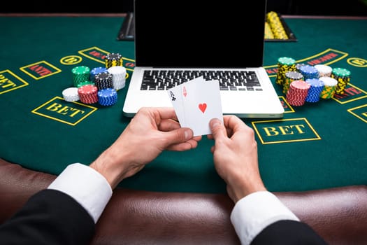 casino, online gambling, technology and people concept - close up of poker player with playing cards, notebook and chips at green casino table. first-person view. two aces, a winning combination