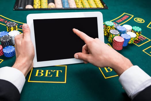casino, online gambling, technology and people concept - close up of poker player with playing cards, tablet and chips at green casino table. first-person view.