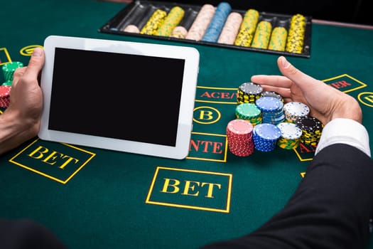 casino, online gambling, technology and people concept - close up of poker player with playing cards, tablet and chips at green casino table. first-person view. takes the prize