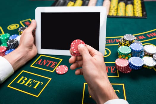 casino, online gambling, technology and people concept - close up of poker player with playing cards, tablet and chips at green casino table. first-person view. It makes chips bet