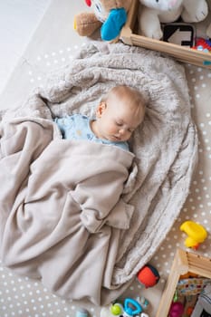 Cute infant baby boy sleeping on playing mat covered with warm cosy blanket