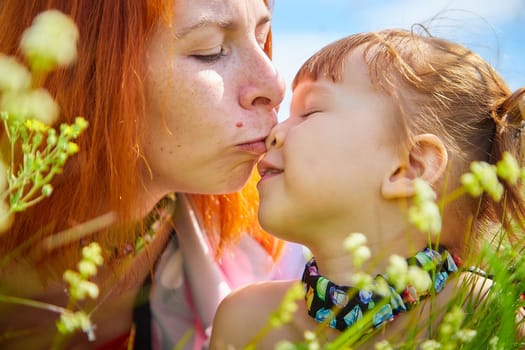 Happy female family with mother and daughter on green and yellow meadow full of grass and flower. Woman with red hair and blonde girl having fun, joy and hug in sunny summer day. Concept family love