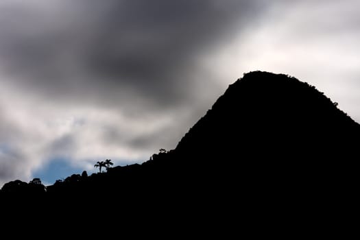 A stunning granite mountain peak stands in silhouette against a dark, impenetrable jungle sky, with space for text.