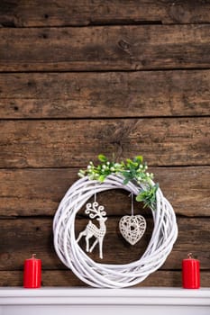 A modest decoration set on a white shelf for the duration of Christmas. Braided wicker garland in the center with a reindeer and a heart.