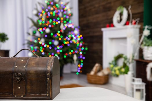 In front you can see an old brown box and against the fuzzy background stands a Christmas tree decorated with glowing Christmas tree lights.
