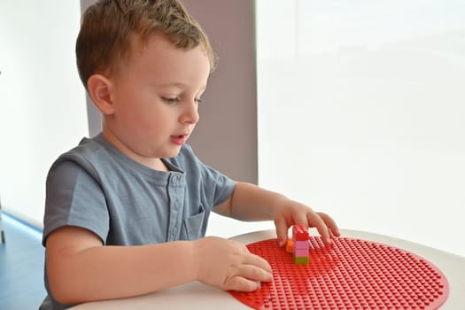 Little child playing with lots of colorful plastic toys indoor, building different cars and objects.