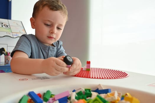 Little child playing with lots of colorful plastic toys indoor, building different cars and objects.