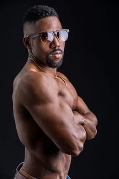 Handsome naked black male bodybuilder posing in studio shot, looking at camera, profile pose, arms crossed on chest