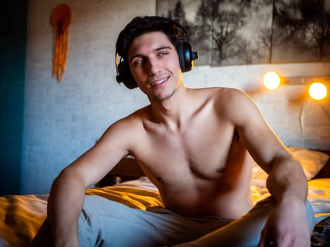 Attractive Young Man Using Headphones Lying Alone On His Bed, Listening to Music and Having a Good Time, Looking at Camera
