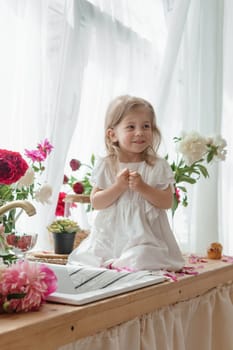 A little blonde girl on a kitchen countertop decorated with peonies. Spring atmosphere