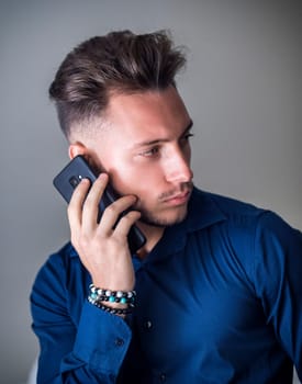 Attractive young man using his mobile phone for a call, on neutral grey background, looking to a side