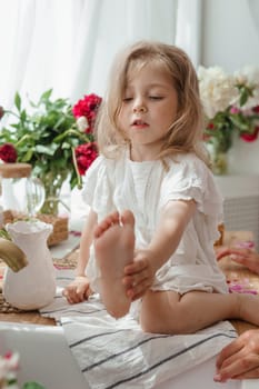 A little blonde girl on a kitchen countertop decorated with peonies. Spring atmosphere